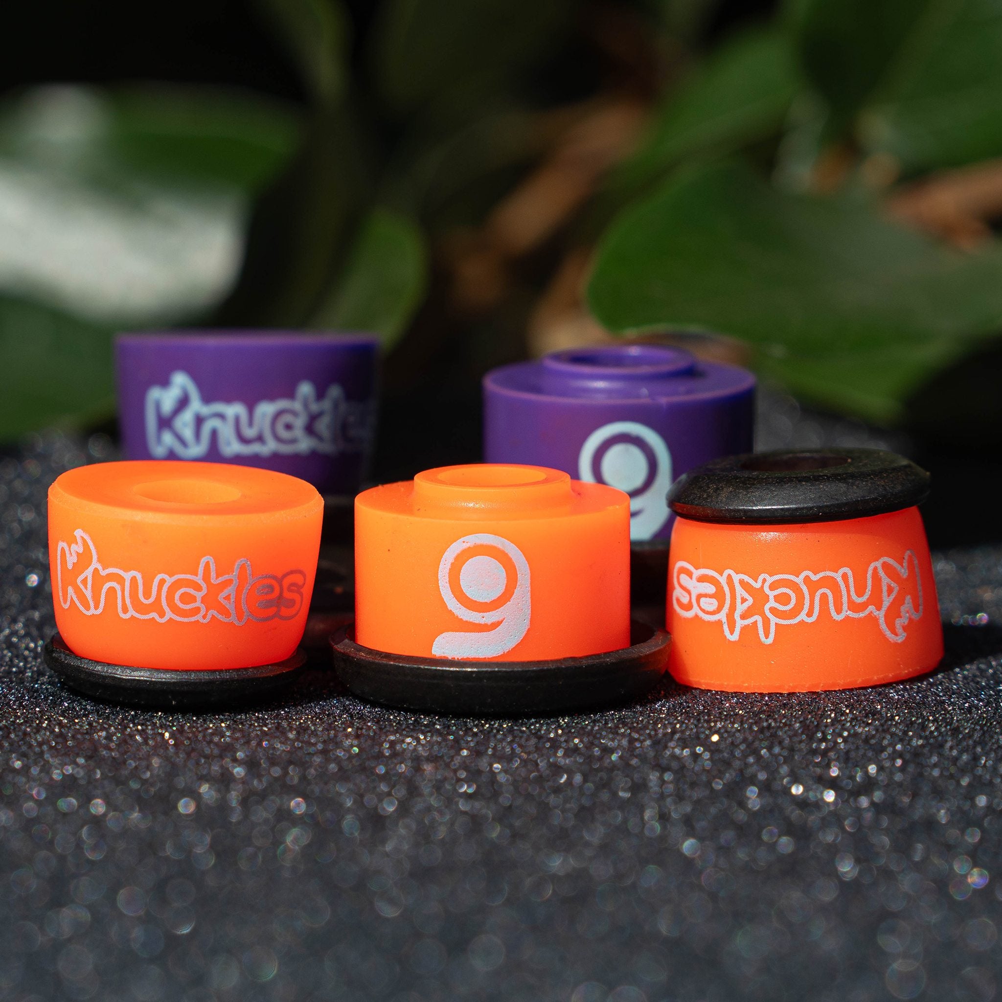 Orangatang Knuckles bushings in orange (soft) and purple (medium) with black washers arranged on grip tape, leaves behind