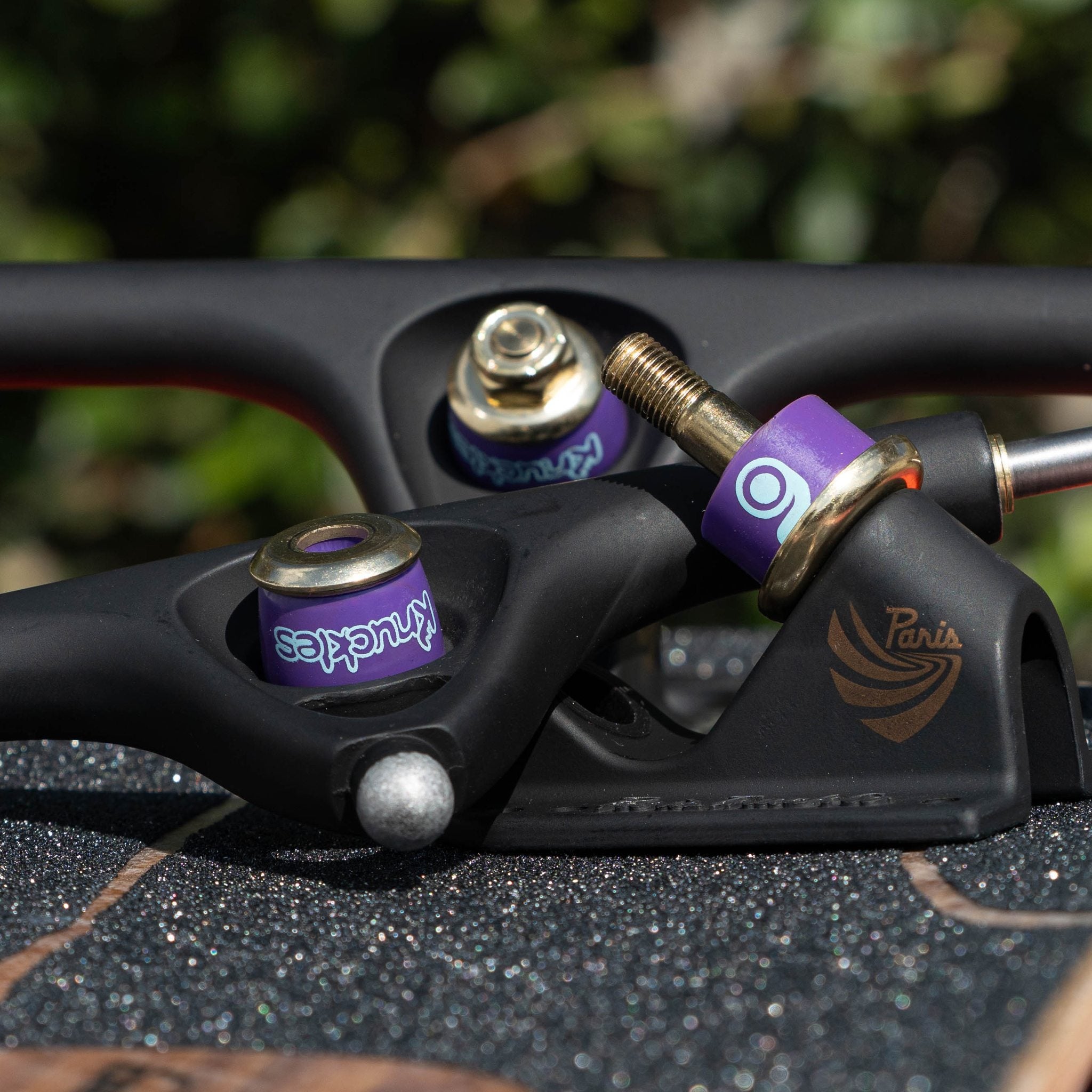 Close-up of purple (medium) Orangatang Knuckles bushings mounted on a black longboard truck with a gold kingpin