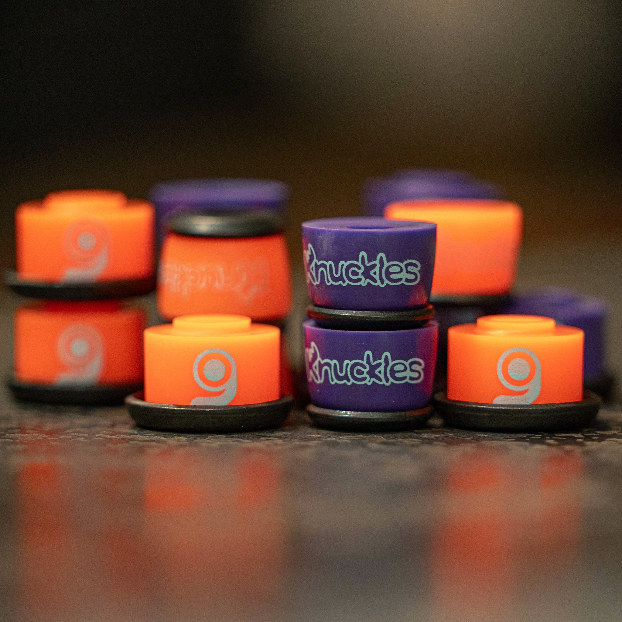 Group of orange (soft) and purple (medium) Orangatang Knuckles bushings with black washers standing on a wooden surface