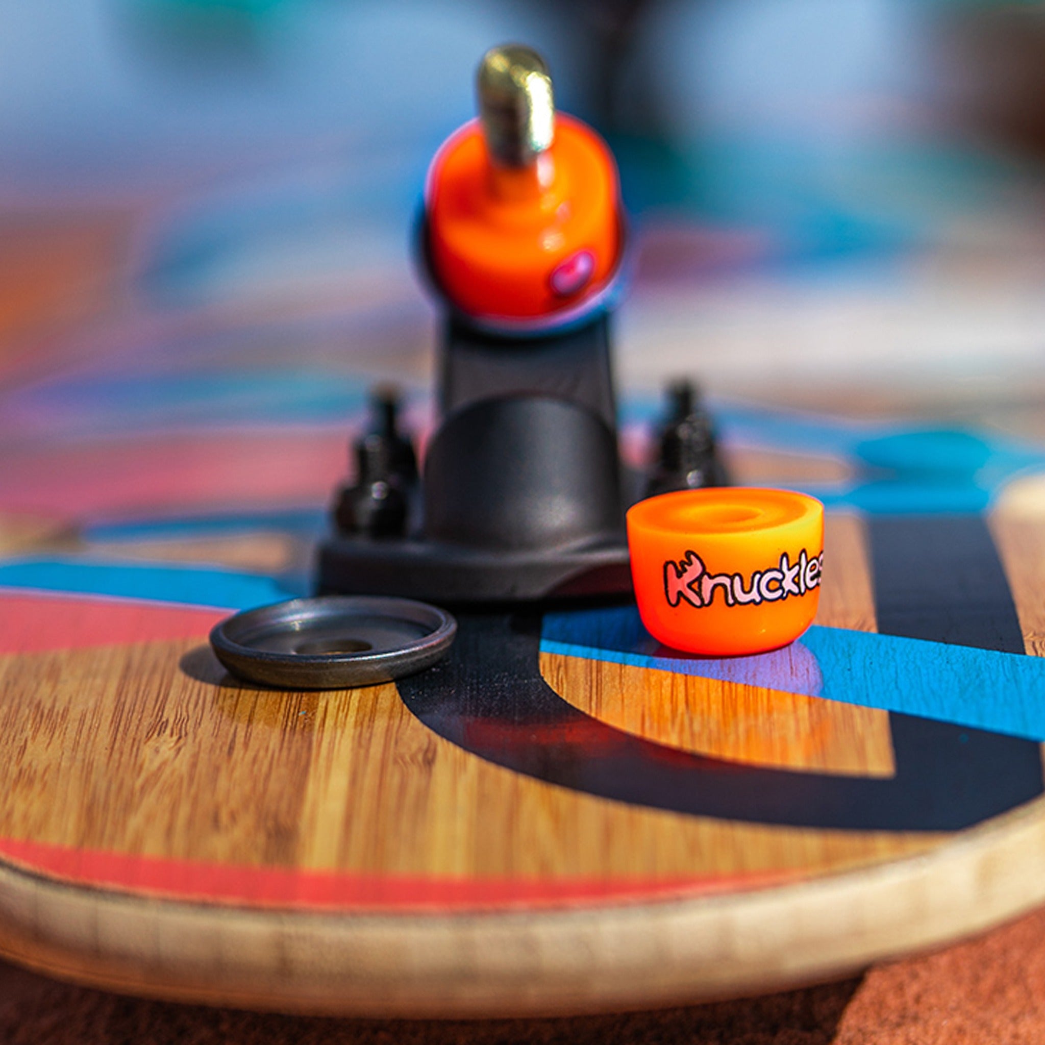 Orange (soft) Orangatang Knuckles bushing on a longboard truck with a loose bushing and washer resting on the painted deck