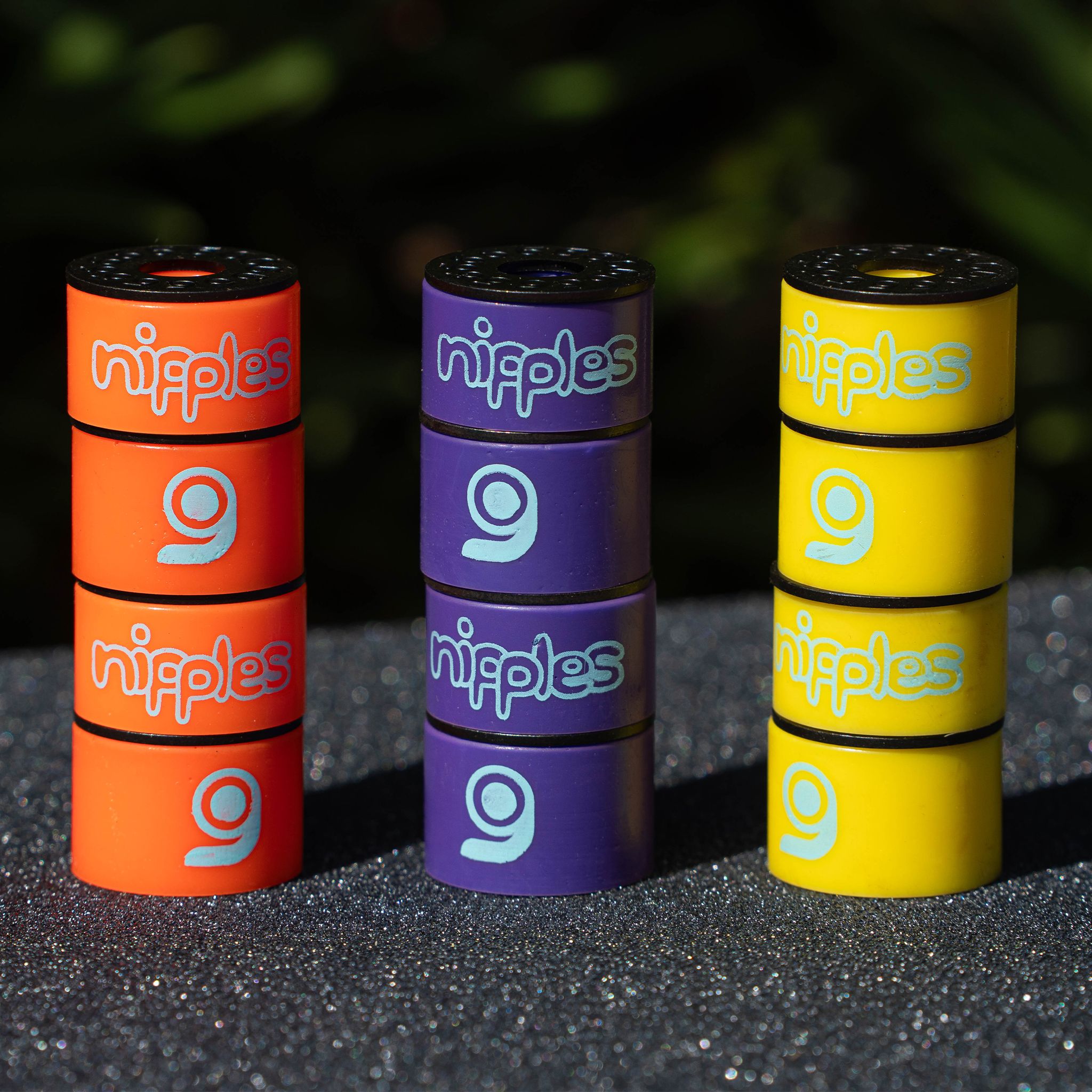 Three stacks of Orangatang Nipples barrel bushings in orange (soft), purple (medium), and yellow (hard) standing on grip tape