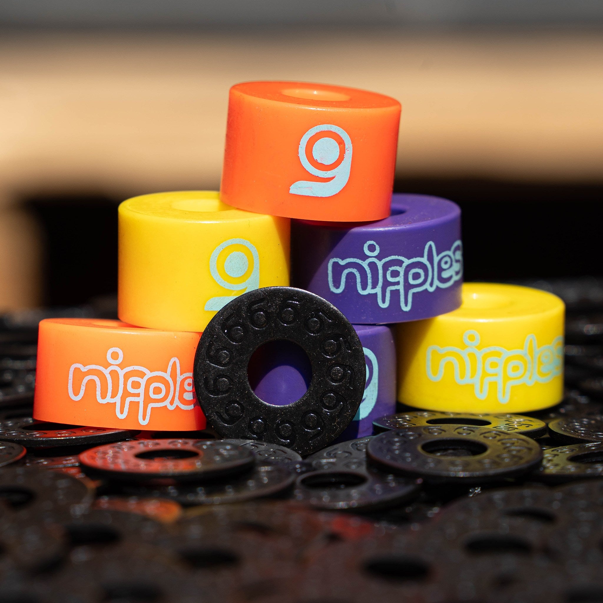 Pile of Orangatang Nipples bushings in orange (soft), yellow (hard), and purple (medium) with black cupped washers on grip tape
