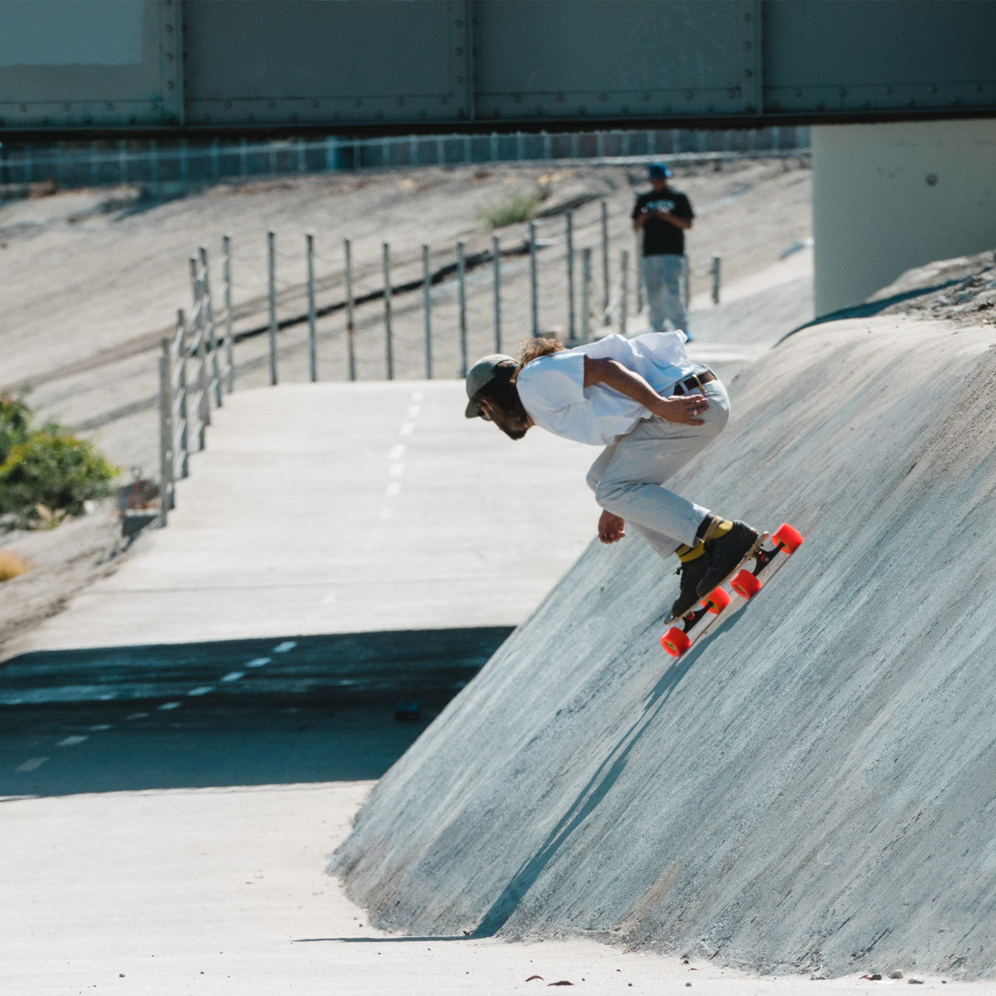 Skater carving up the sloped concrete bank of a drainage channel on a longboard with orange Orangatang 4President wheels