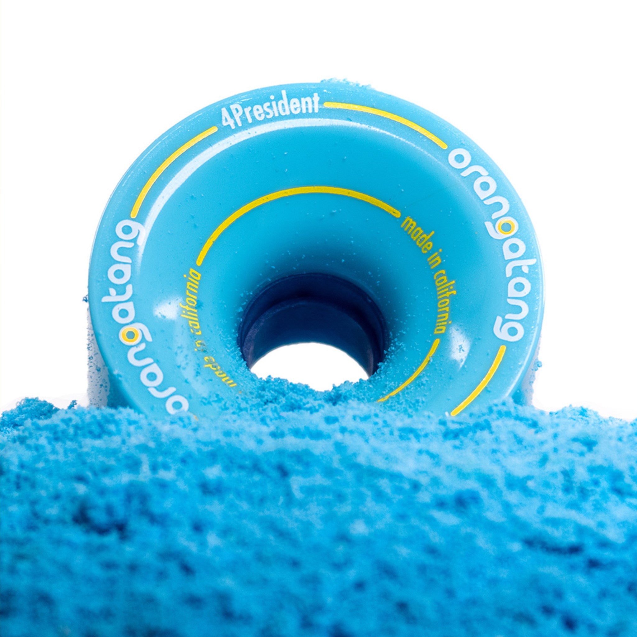 Blue Orangatang 4President 70mm longboard wheel standing upright in a pile of blue powder against a white background