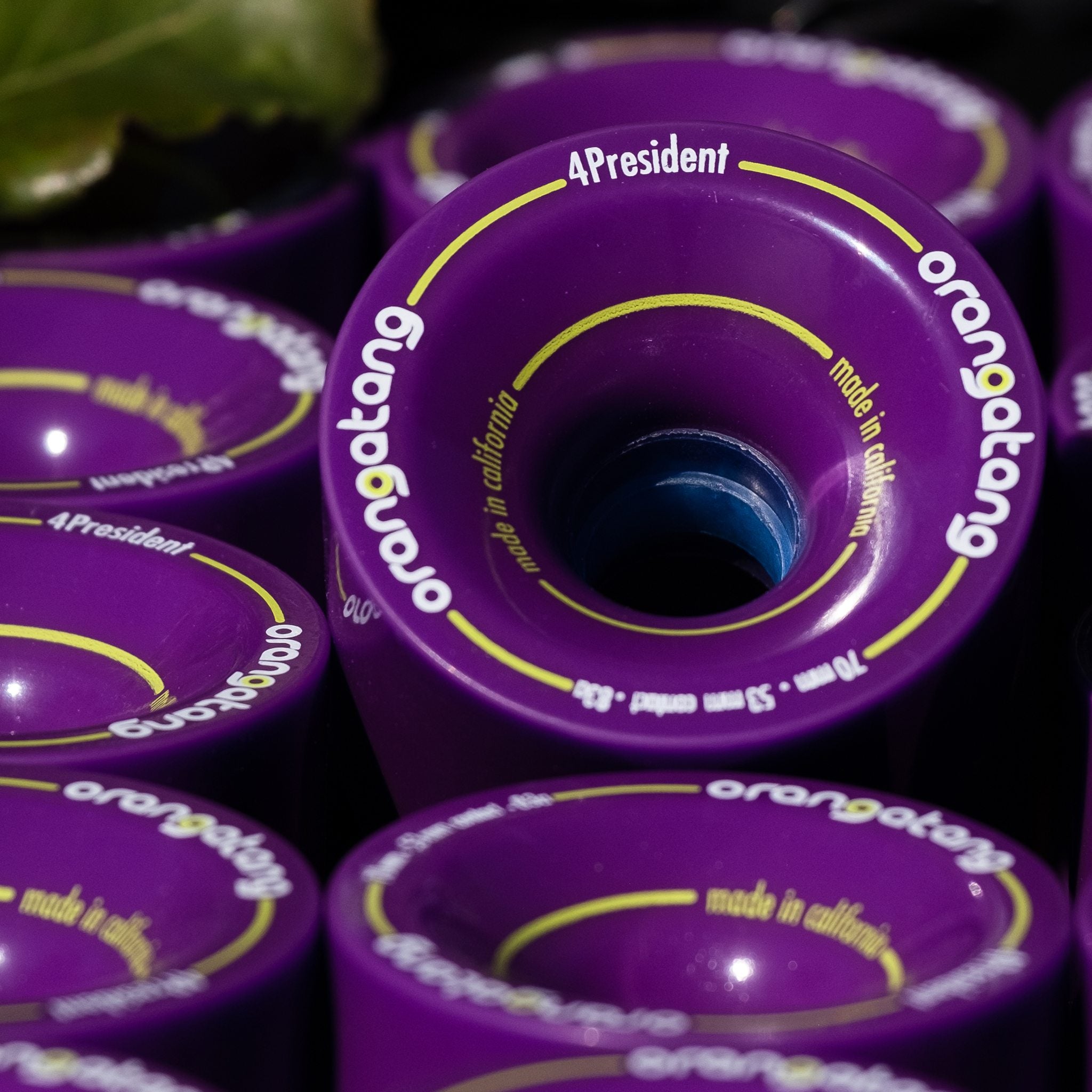 Close-up of stacked purple Orangatang 4President 70mm wheels with yellow logo graphics, made in California