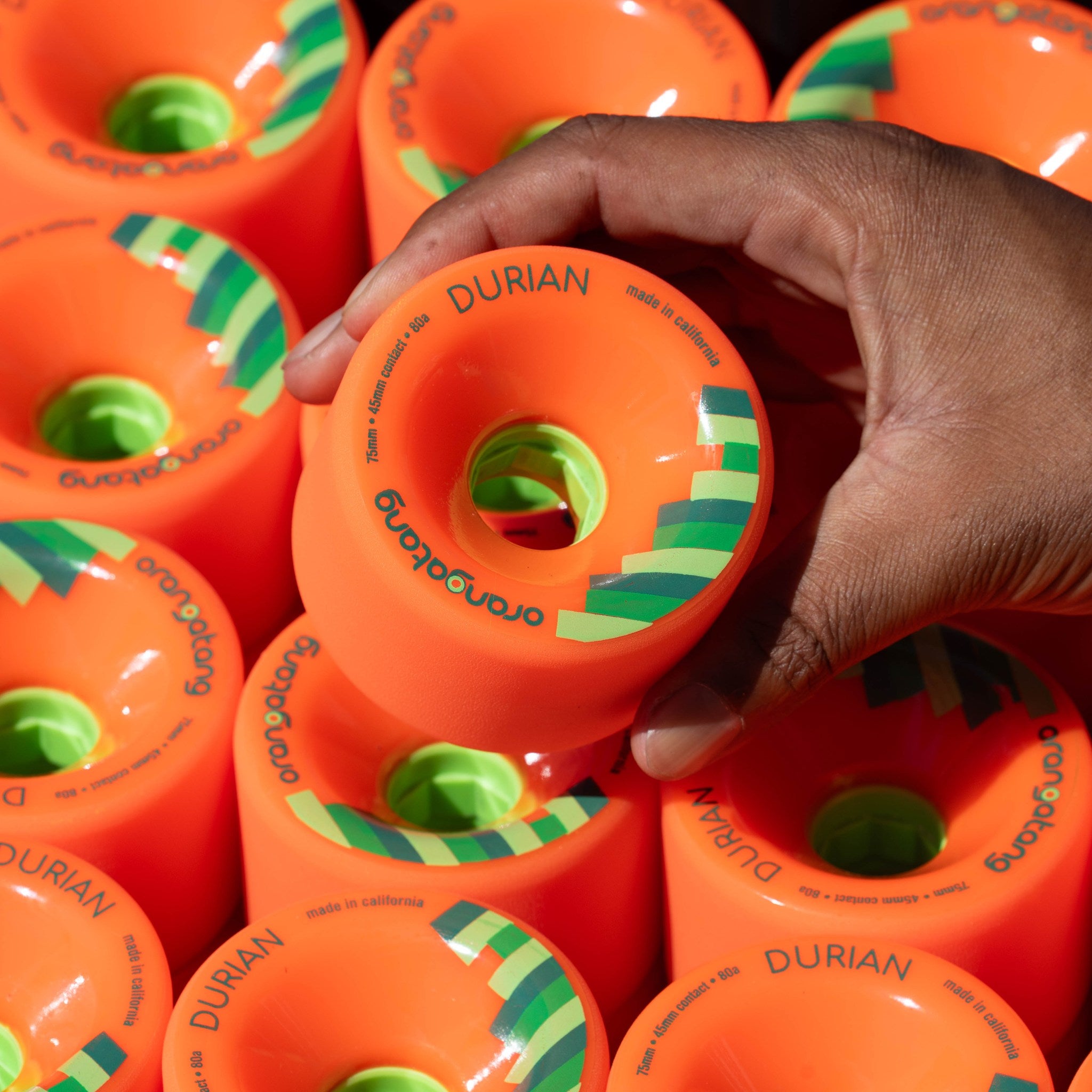 Hand pulling one orange Orangatang Durian 75mm wheel from a tightly packed stack of Durian wheels with green cores