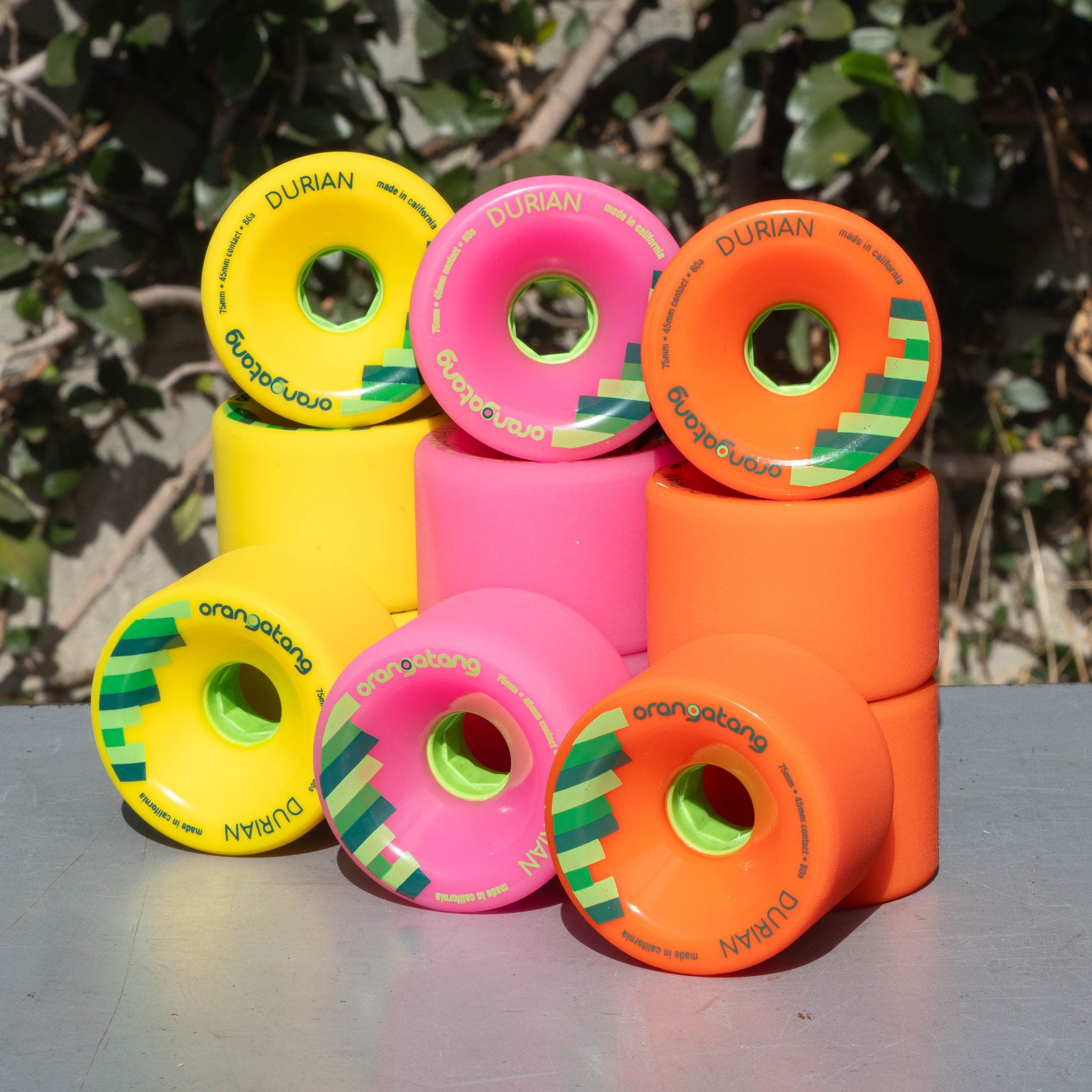 Stacked Orangatang Durian 75mm wheels in yellow, pink, and orange with green cores, photographed outdoors
