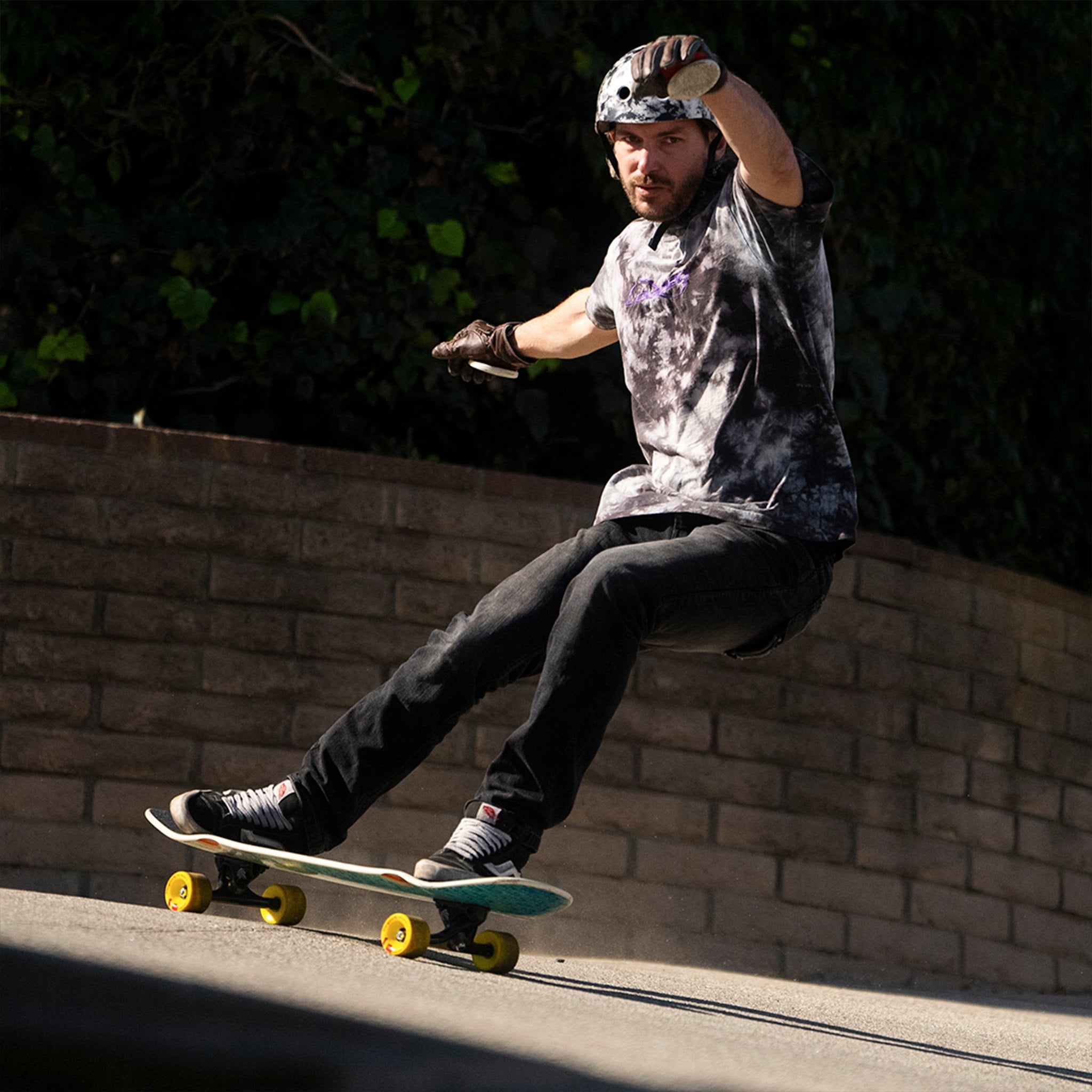 Skater in a helmet and gloves sliding a small board with yellow Orangatang Fat Free 65mm wheels beside a brick wall