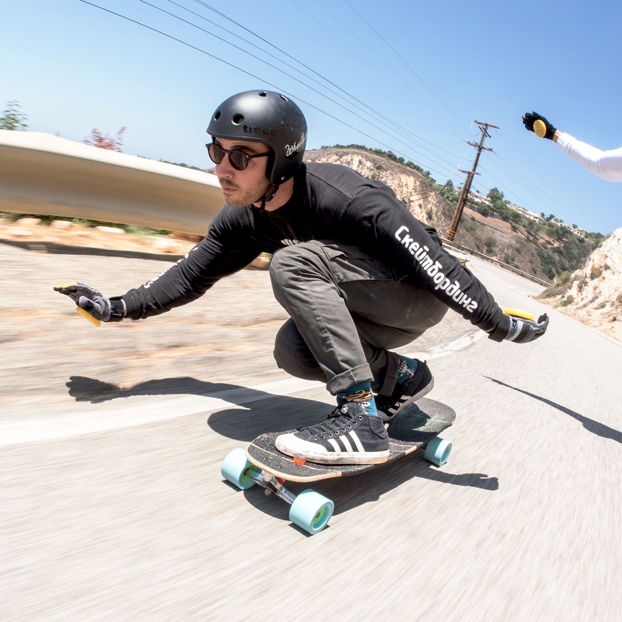 Downhill skater in a helmet and gloves in a tucked carve on a longboard with light blue Orangatang Kegel 80mm wheels