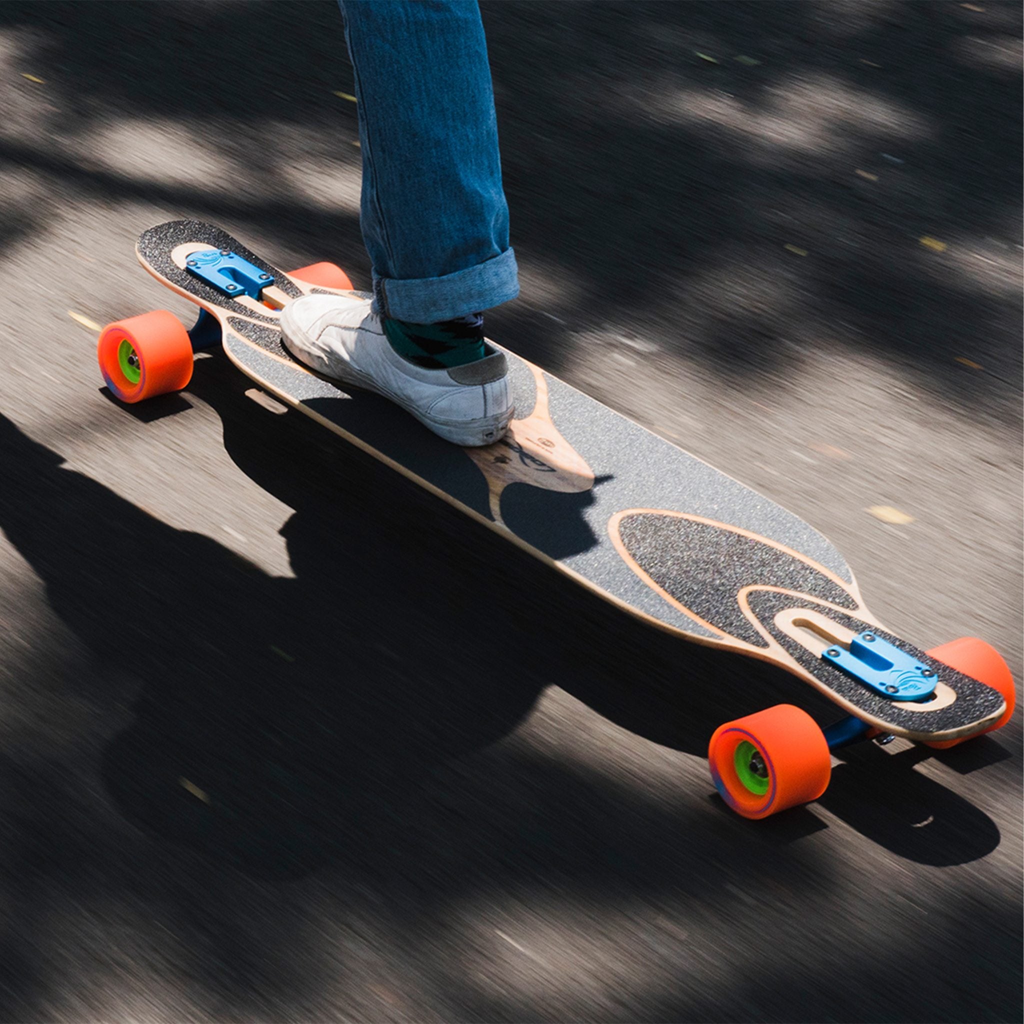 Rider cruising a drop-through longboard on orange Orangatang Kegel 80mm wheels, viewed from above with motion blur