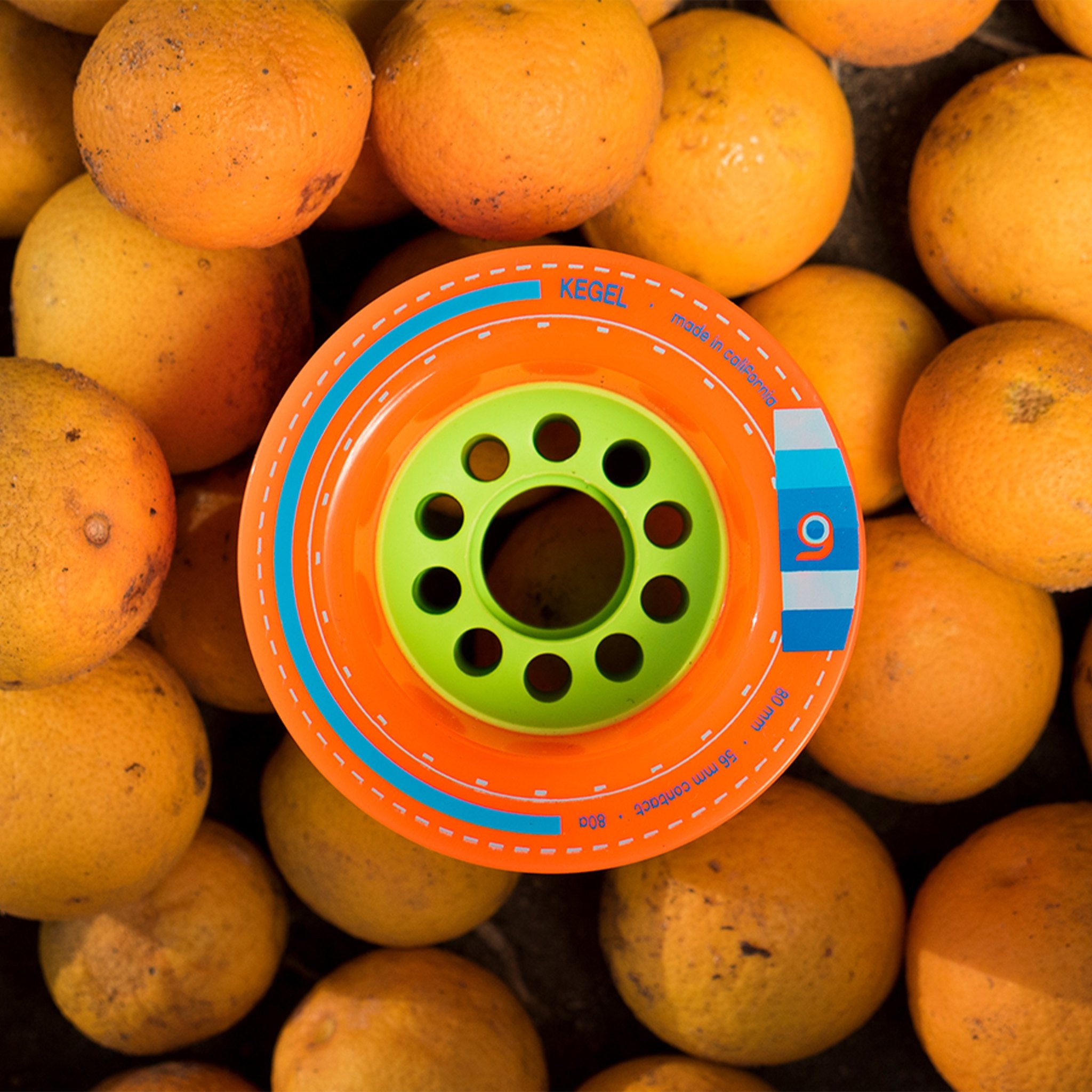 Orange Orangatang Kegel 80mm wheel with green core lying on a bed of fresh oranges