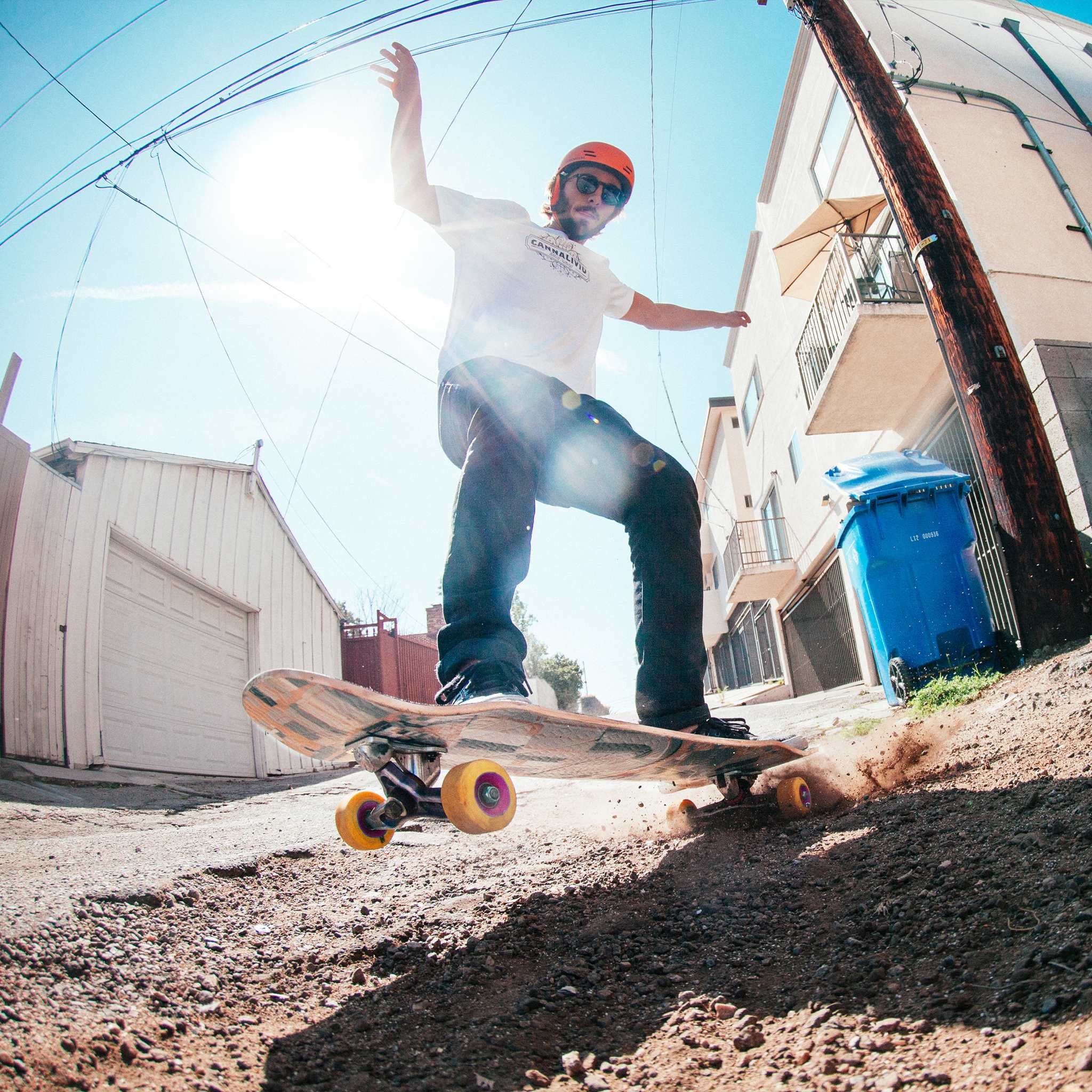 Low-angle view of a skater in a helmet sliding a cruiser board with yellow Orangatang Skiff 62mm wheels in a sunny alley