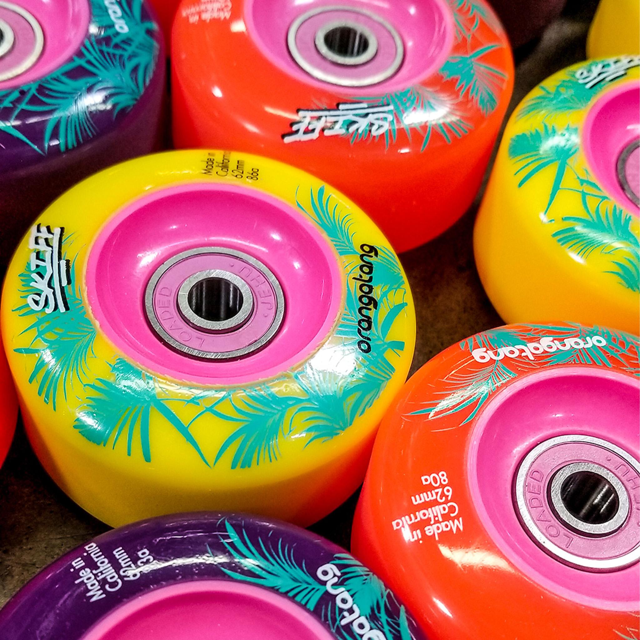 Close-up of Orangatang Skiff 62mm wheels in yellow, orange, and purple with pink cores and teal palm leaf graphics